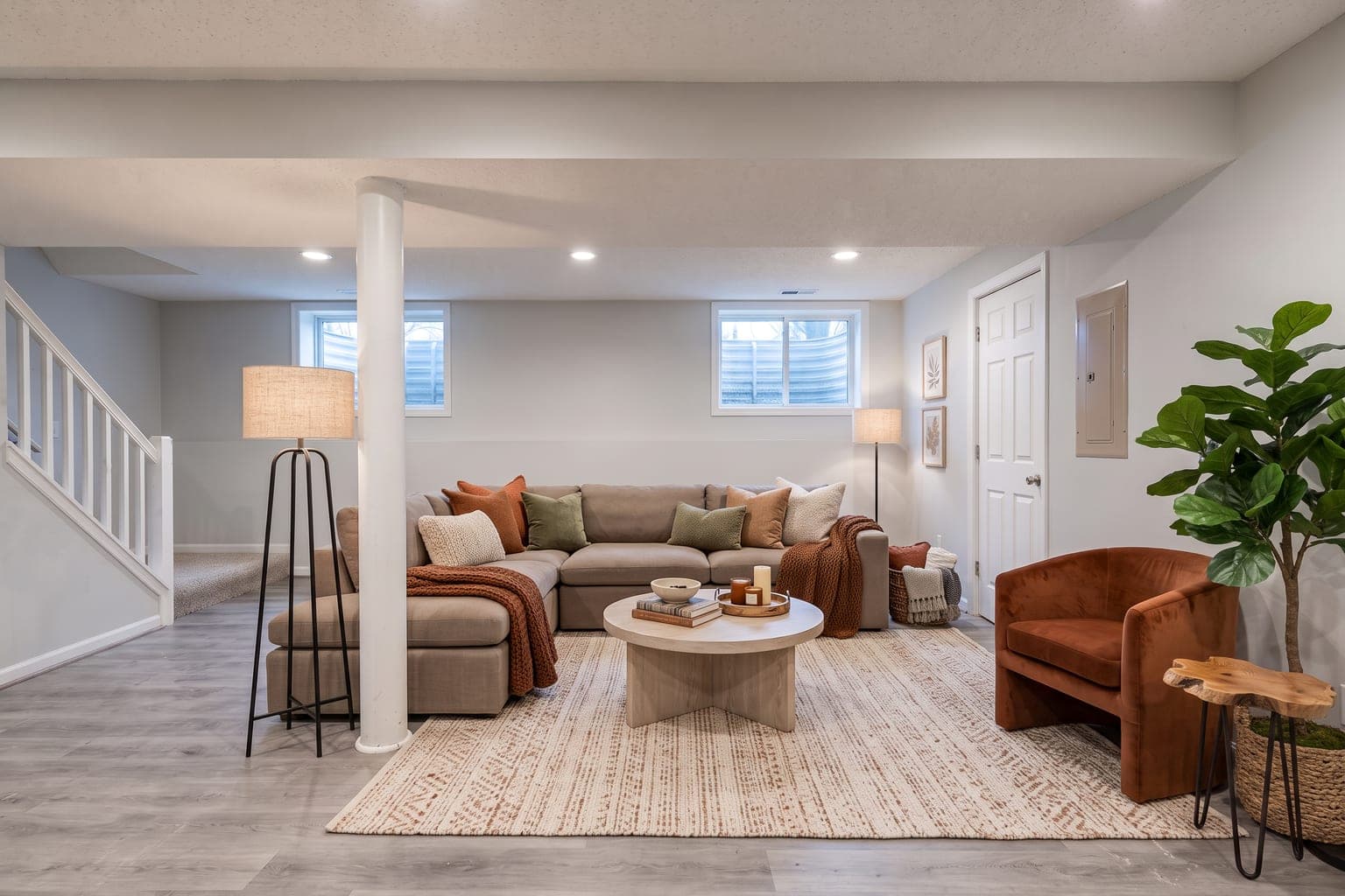 Finished basement virtually staged with AI as a family room - gray sectional, round coffee table, rust accent chair, floor lamp, rug and a plant