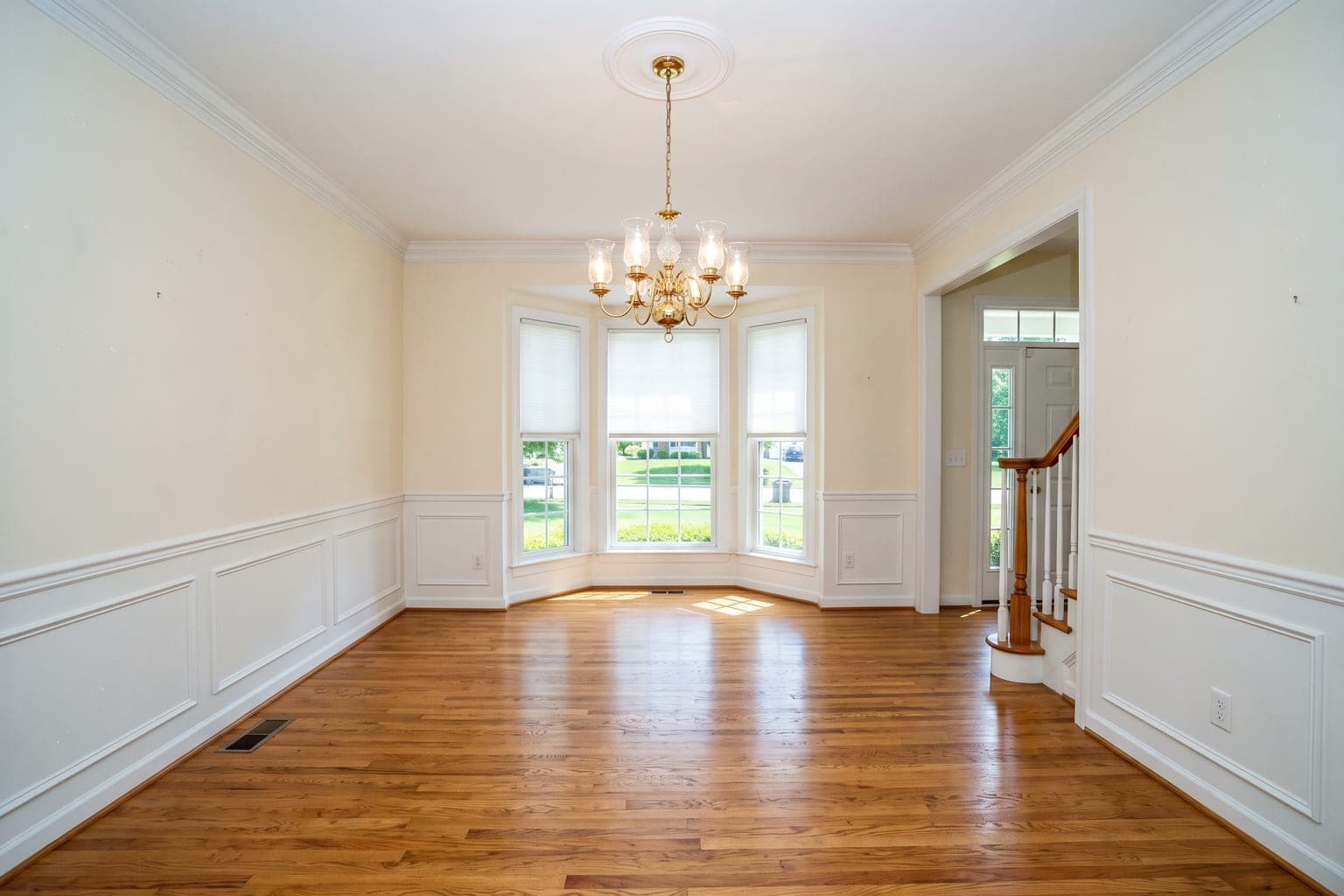 Empty formal dining room before virtual staging - wainscoting, brass chandelier, bay window, oak floors