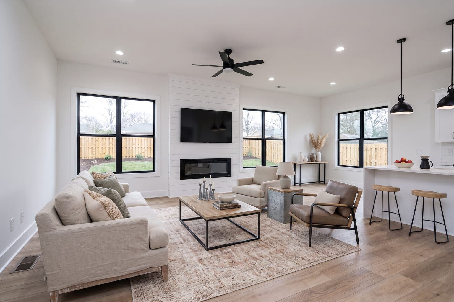 Family room virtually staged with AI in modern farmhouse style - light sofa, wood-and-metal coffee table, two armchairs and a woven rug