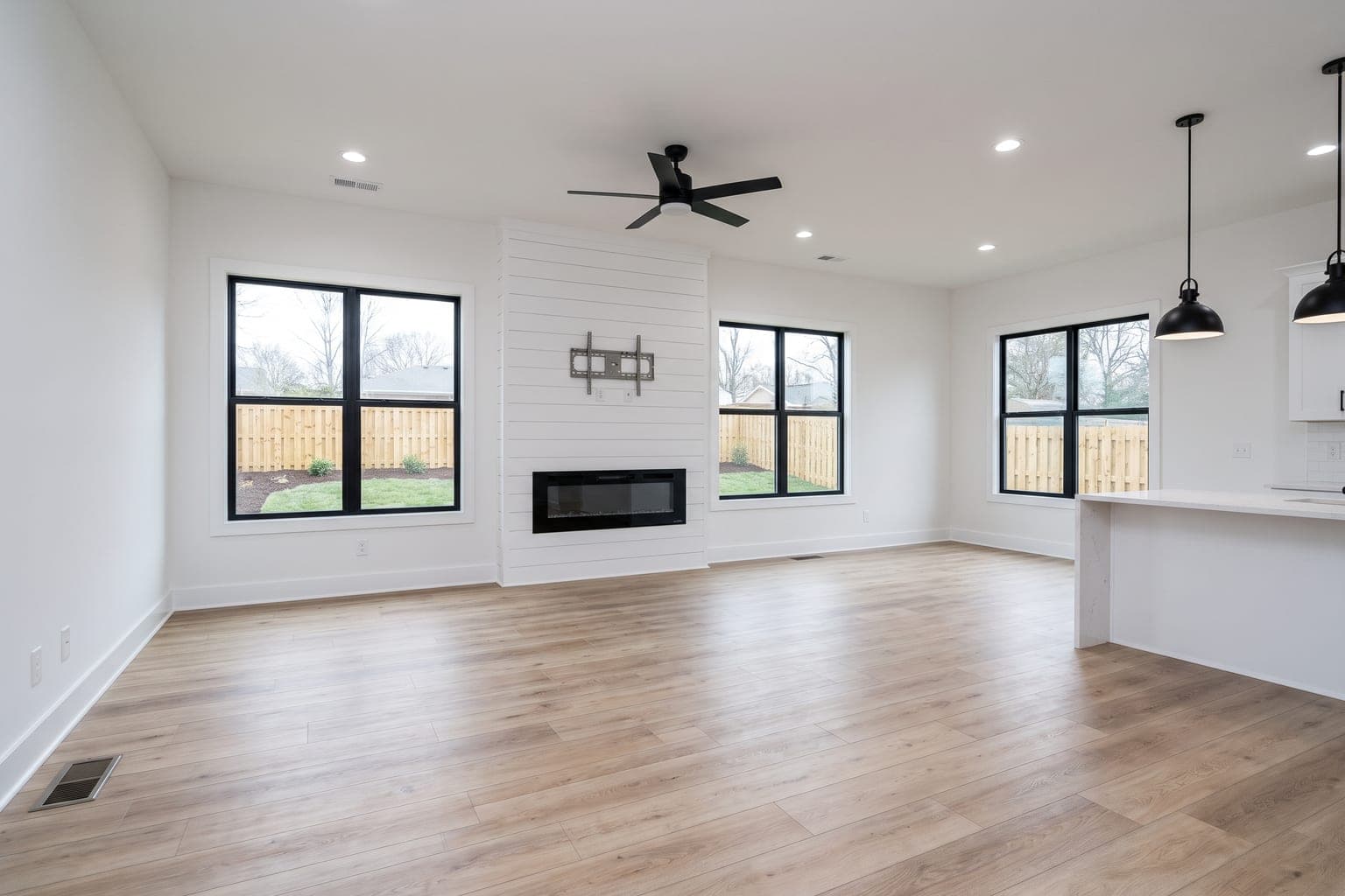 Empty new-construction family room before virtual staging - shiplap fireplace wall, black-framed windows, light oak floor