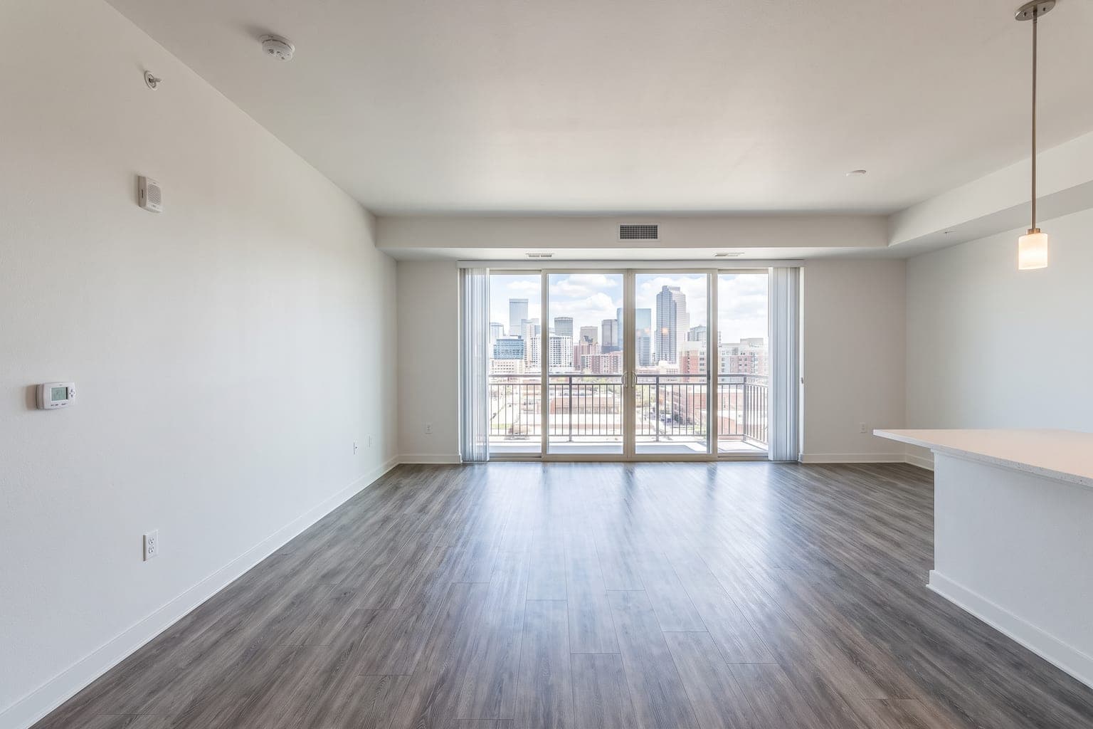 Empty open-concept condo living and dining area before virtual staging - vinyl plank floor, balcony door, kitchen peninsula
