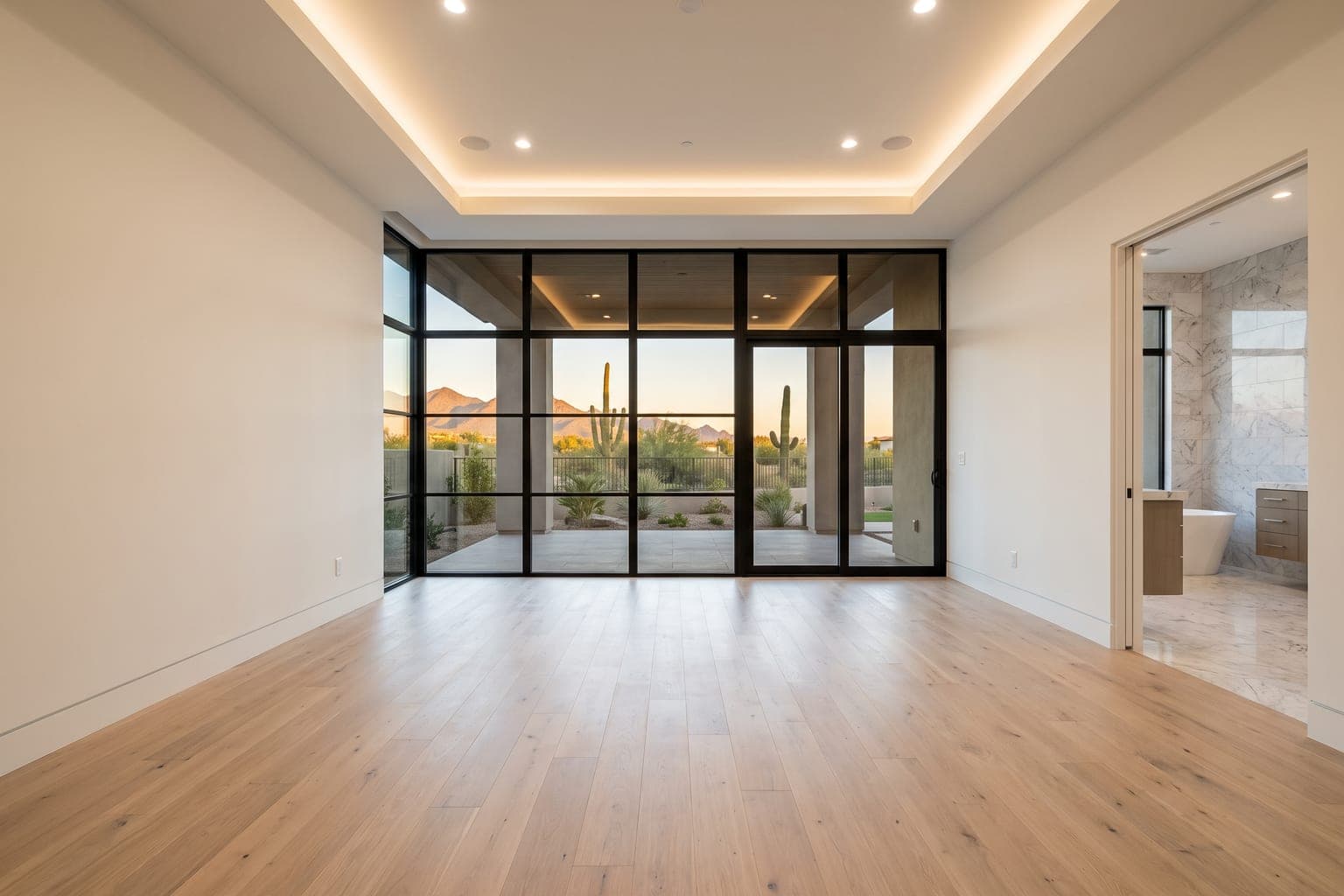 Empty luxury primary suite before virtual staging - white oak floor, tray ceiling, steel-framed windows to a desert patio