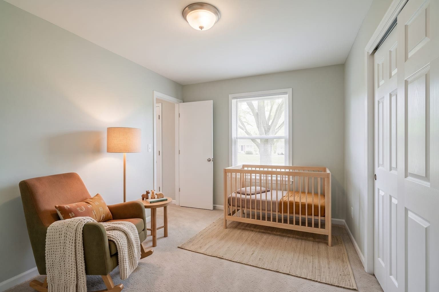 Small bedroom virtually staged with AI as a nursery - natural wood crib, glider, floor lamp, side table and a soft rug