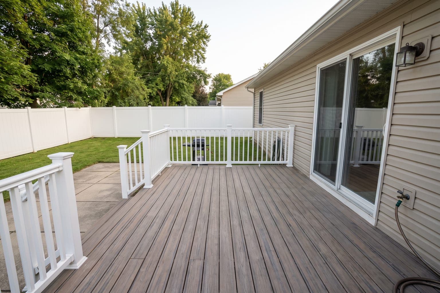 Empty composite backyard deck before virtual staging - white vinyl railing, sliding door, lawn and privacy fence