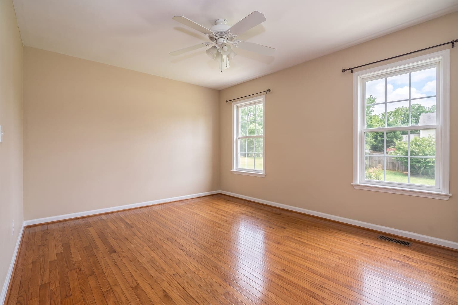 The same family room after AI furniture removal - empty, with the hardwood floor and walls rebuilt, ceiling fan and curtains unchanged