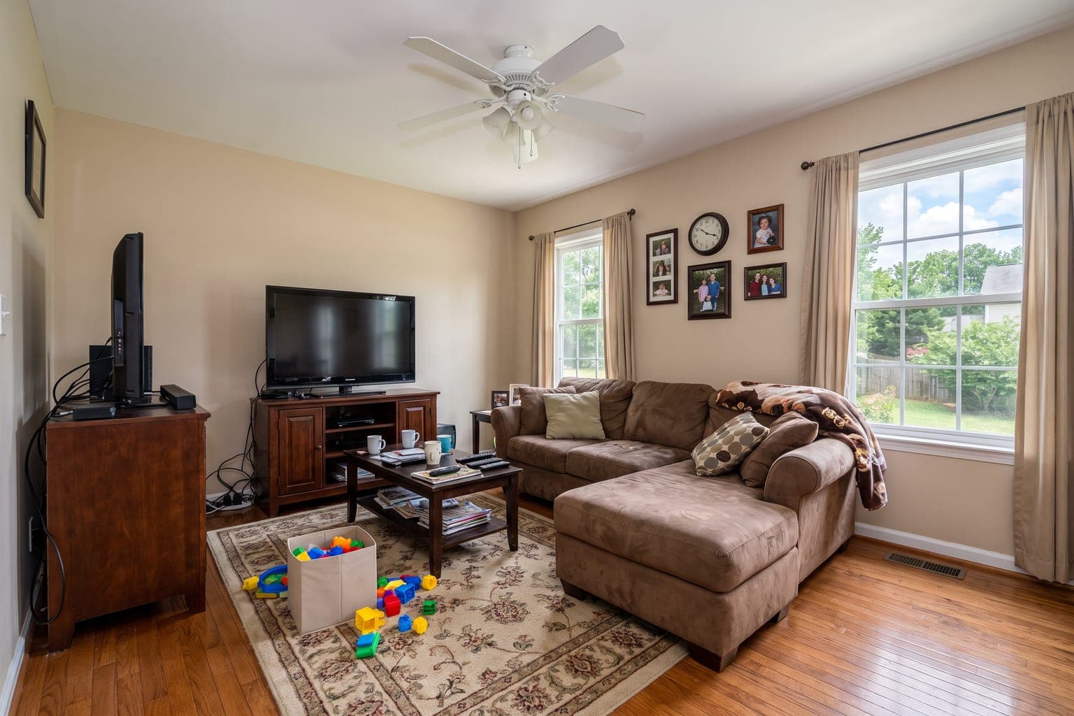 Lived-in family room before AI furniture removal - brown sectional, TV cabinet, toys and clutter on oak floors