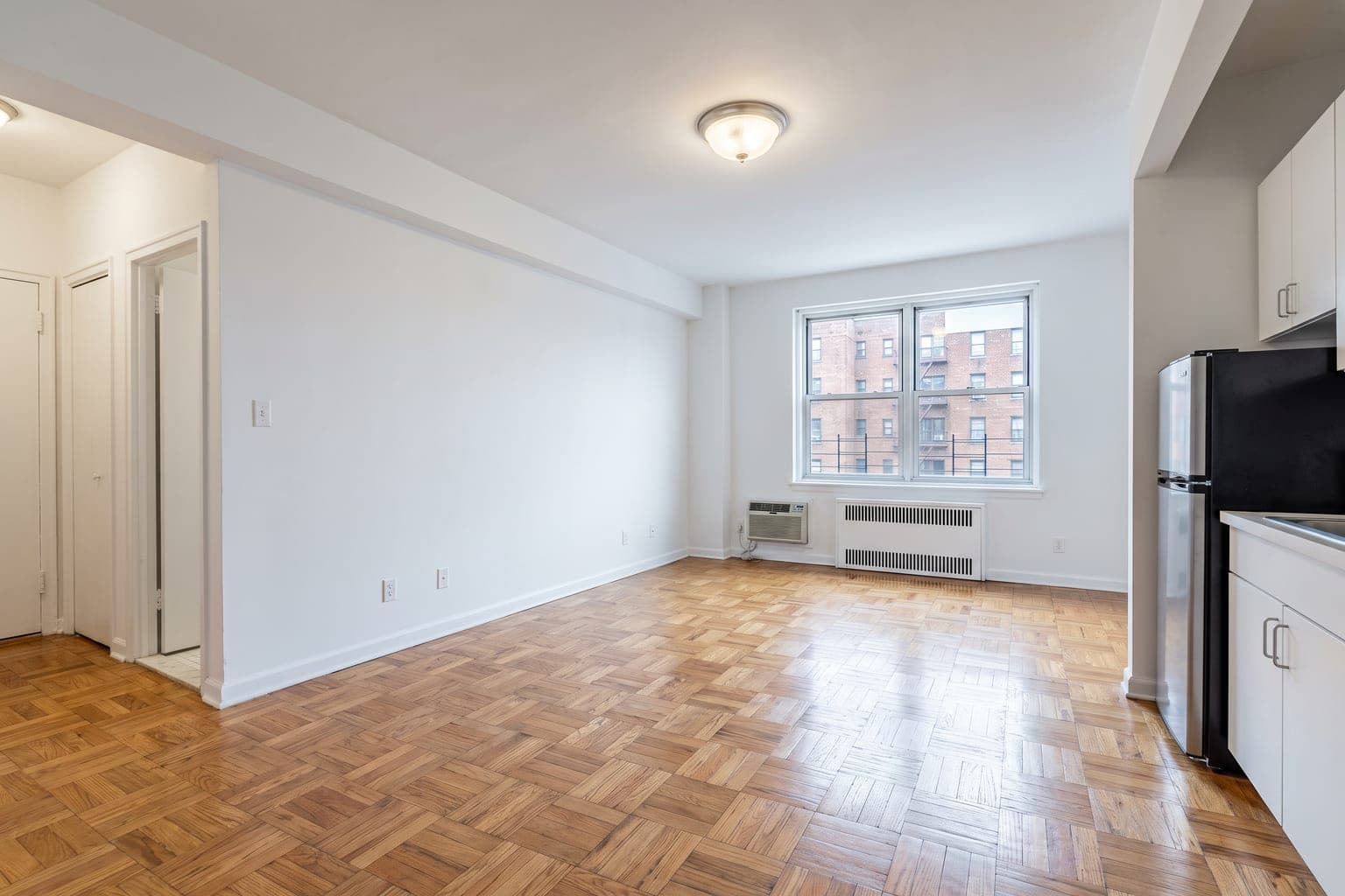 Empty studio apartment before virtual staging - parquet floor, radiator under the window, galley kitchenette