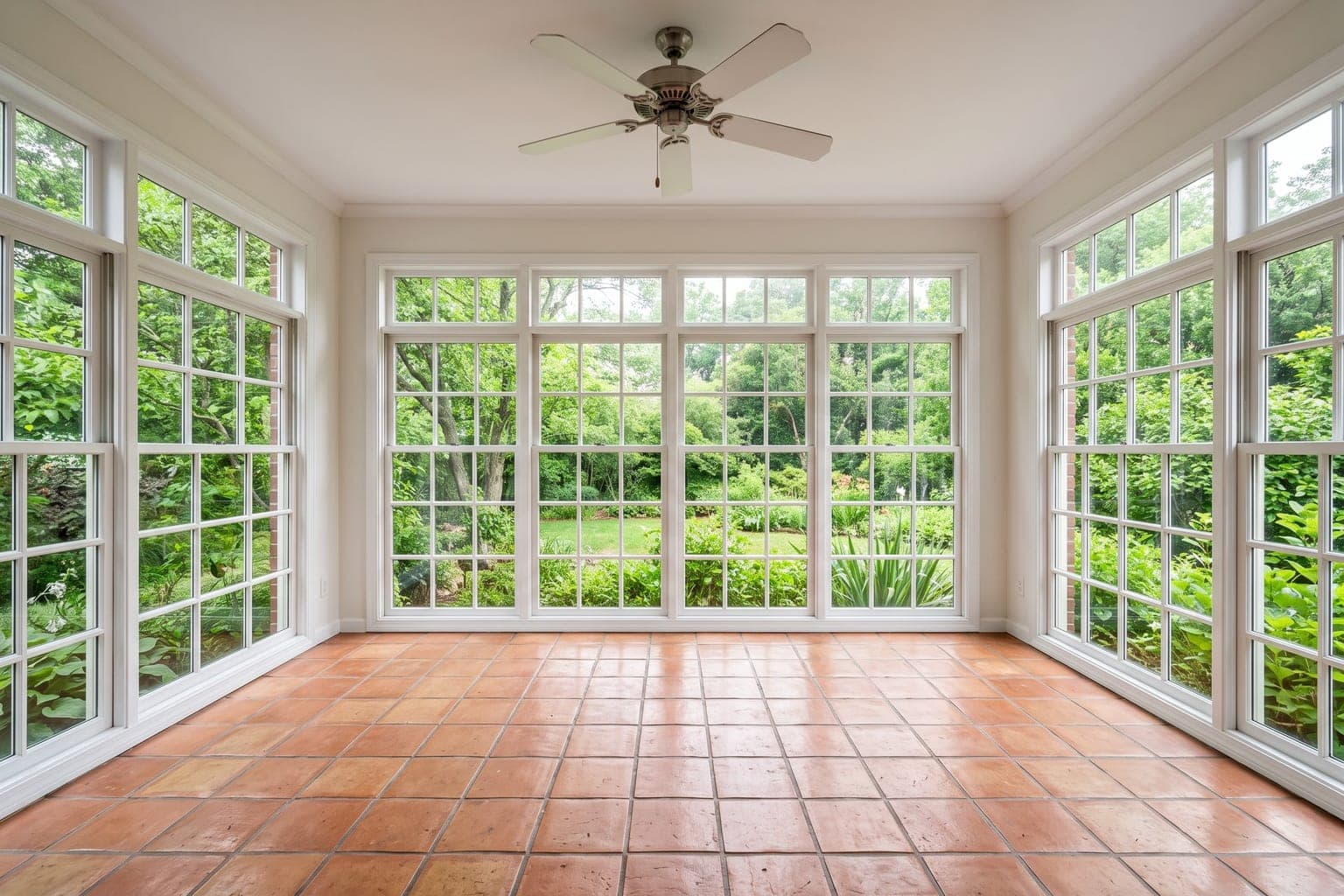 Empty sunroom before virtual staging - terracotta tile floor, floor-to-ceiling windows on three sides, ceiling fan