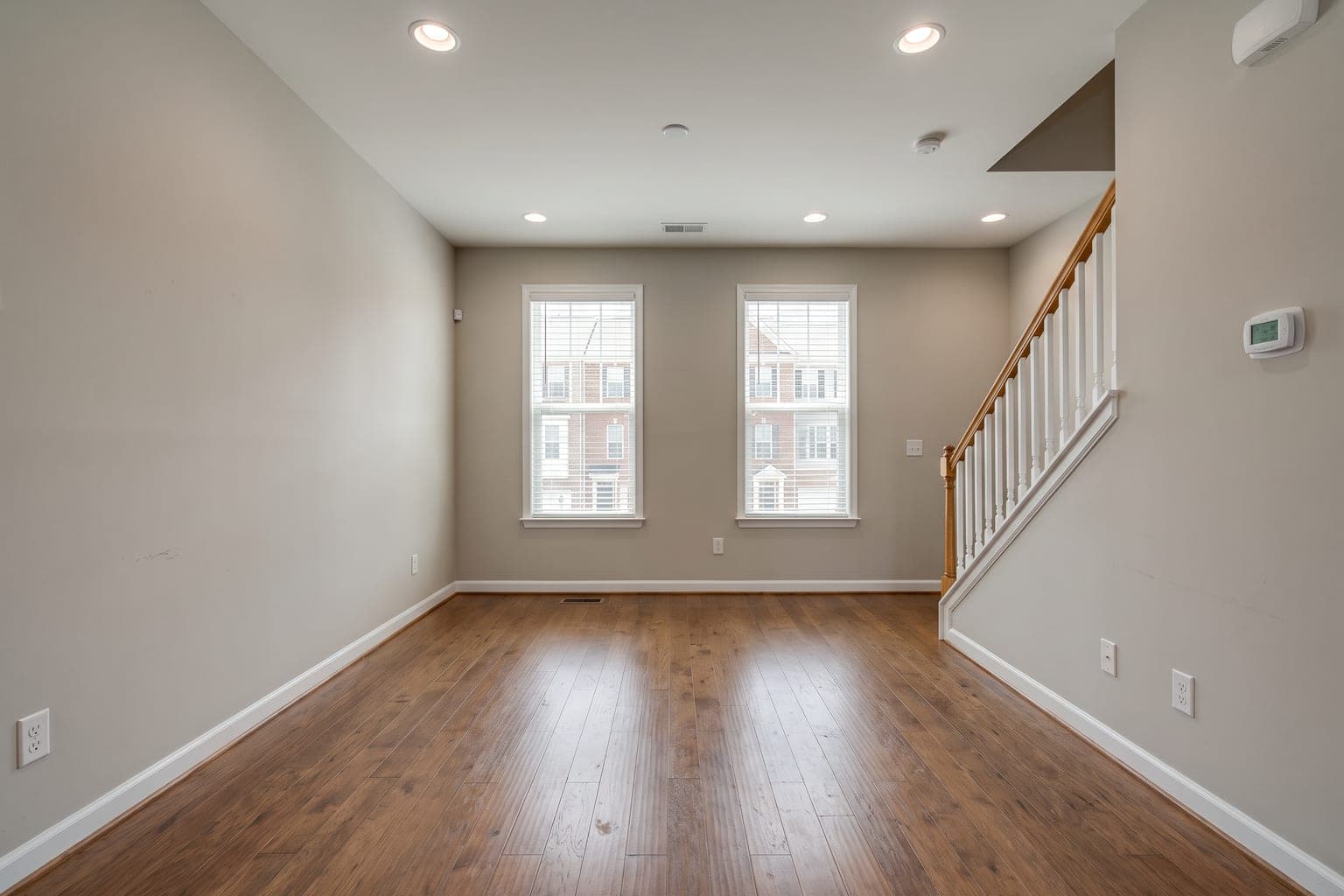 Empty townhouse living room before digital staging - engineered hardwood, tall windows, open staircase